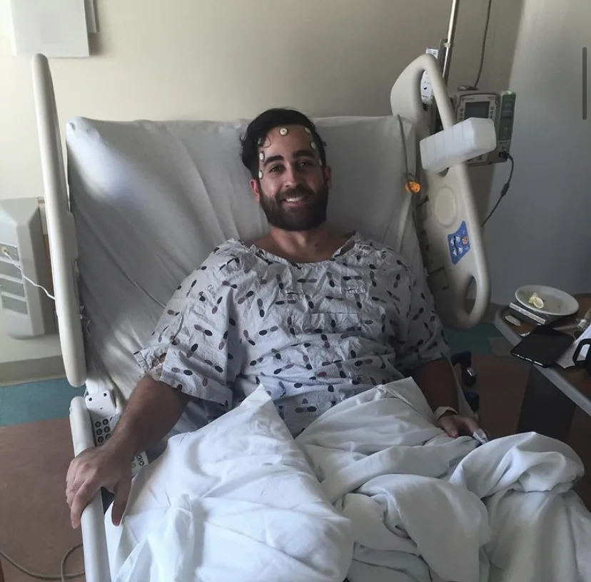 Alex smiling from a hospital bed during treatment for a brain tumor.